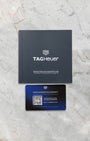 The official black TAG Heuer instruction guide manual and modern plastic smart international warranty card on a marble surface
