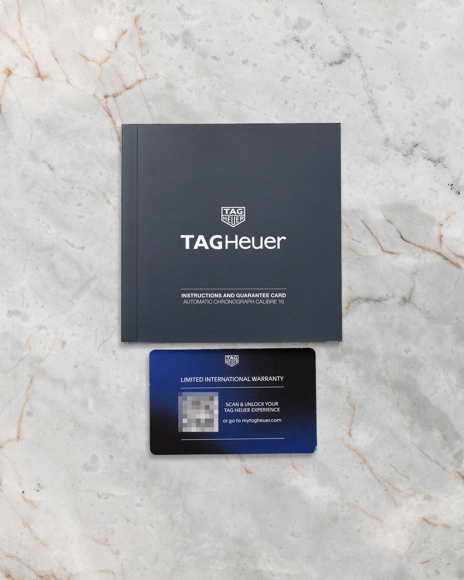 The official black TAG Heuer instruction guide manual and modern plastic smart international warranty card on a marble surface