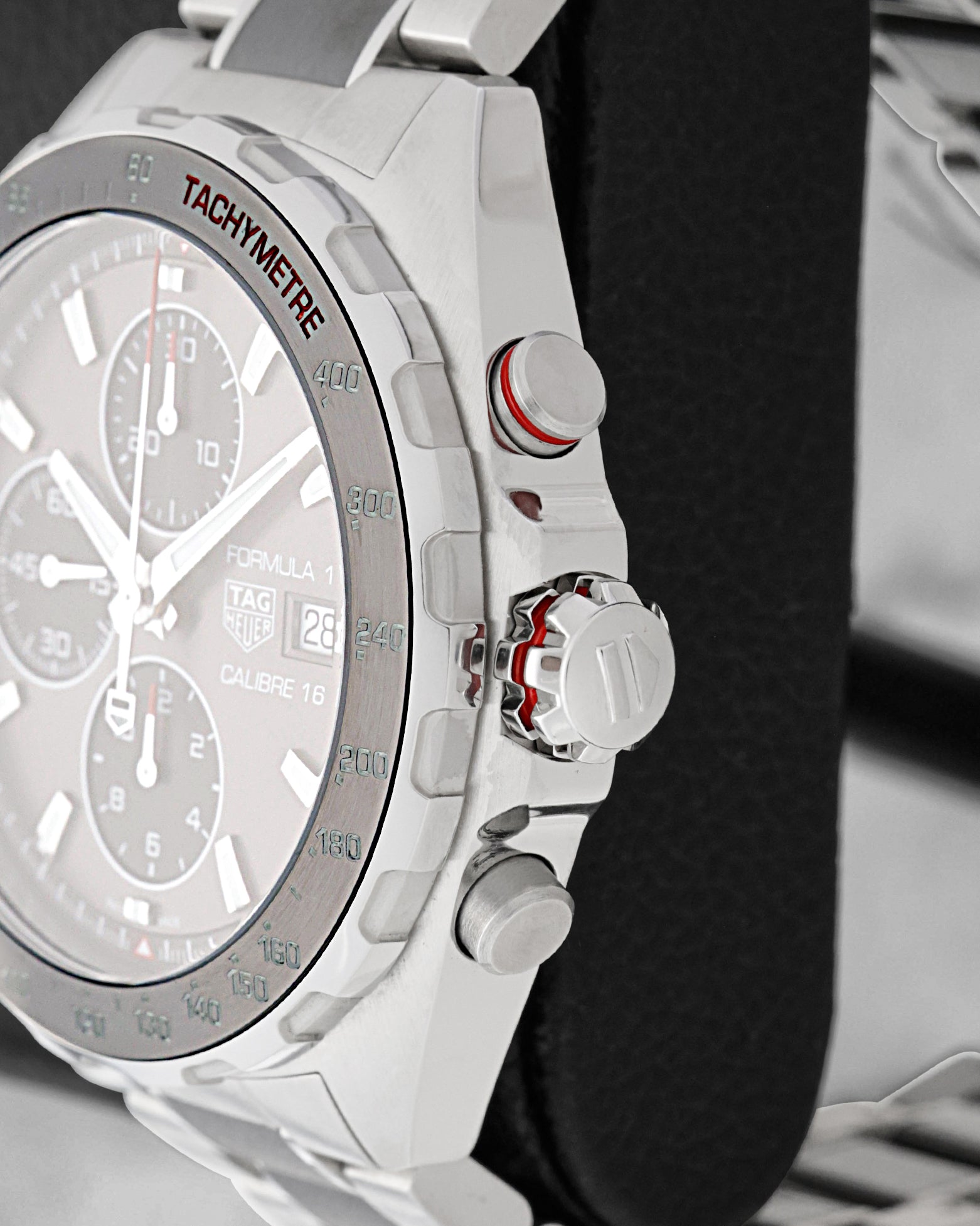 Close-up side view of screw-down crown, red-trimmed chronograph pusher, and black tachymeter bezel on TAG Heuer F1