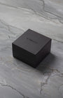 A closed square dark brown TAG Heuer luxury watch presentation box sitting centered on a textured grey marble surface