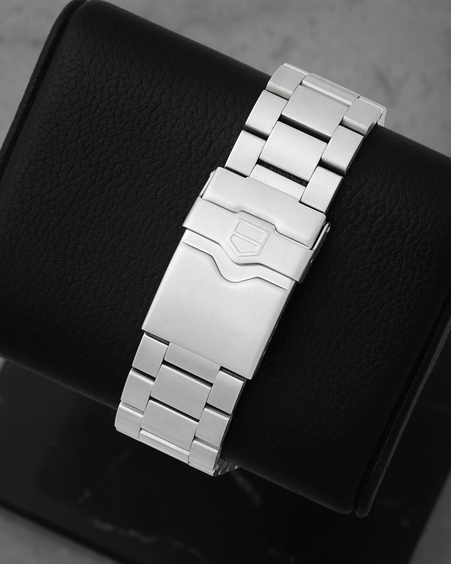 Rear studio view of the brushed three-link stainless steel watch bracelet and folding double-security clasp with the engraved TAG Heuer shield