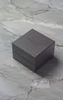 A closed square dark brown TAG Heuer luxury watch presentation box sitting on a textured grey marble background