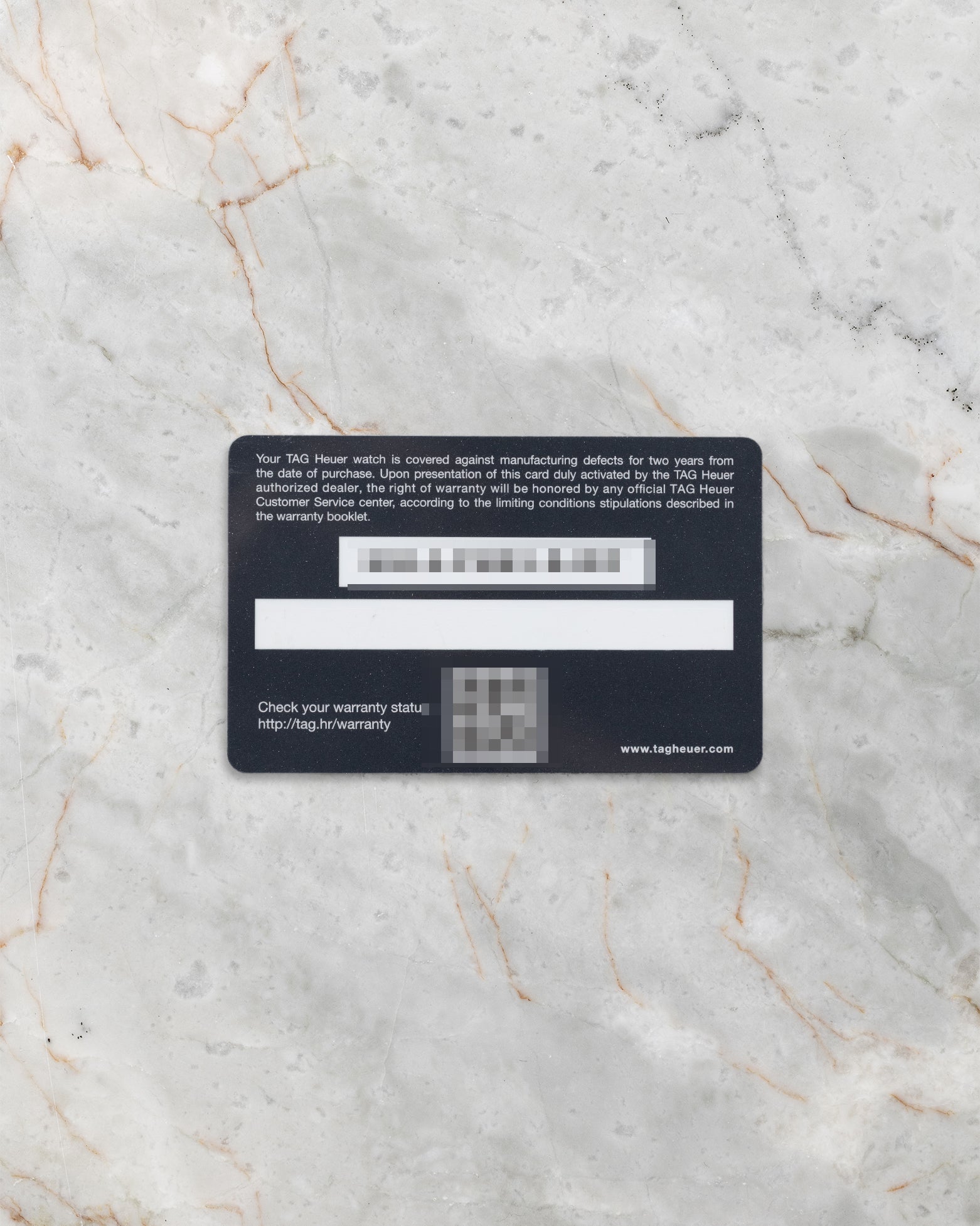 back view of the official TAG Heuer plastic international warranty card showing its magnetic strip flat-laid on light gray marble