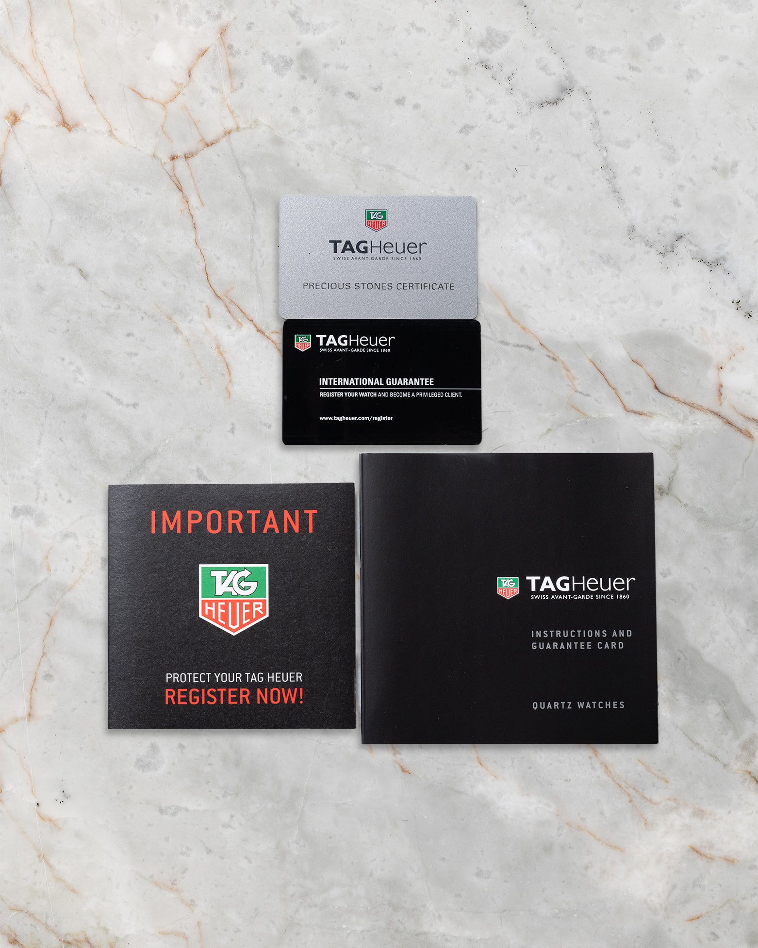 Official TAG Heuer international guarantee card displayed alongside the red registration reminder insert and black leatherette owner instruction handbook manual