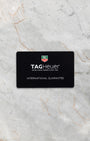 The official black TAG Heuer international guarantee warranty card displayed flat on a light marble background