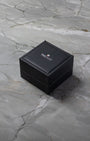 A closed square dark brown TAG Heuer luxury watch presentation box sitting centered on a textured grey marble background