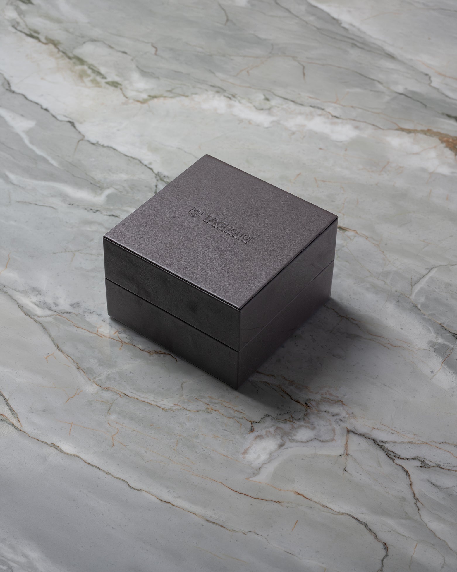 A closed brown TAG Heuer luxury watch presentation box sitting on a textured grey marble surface.