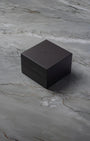 A top-down three-quarter angle of the official square black textured leatherette TAG Heuer watch presentation box resting on a grey marble backdrop