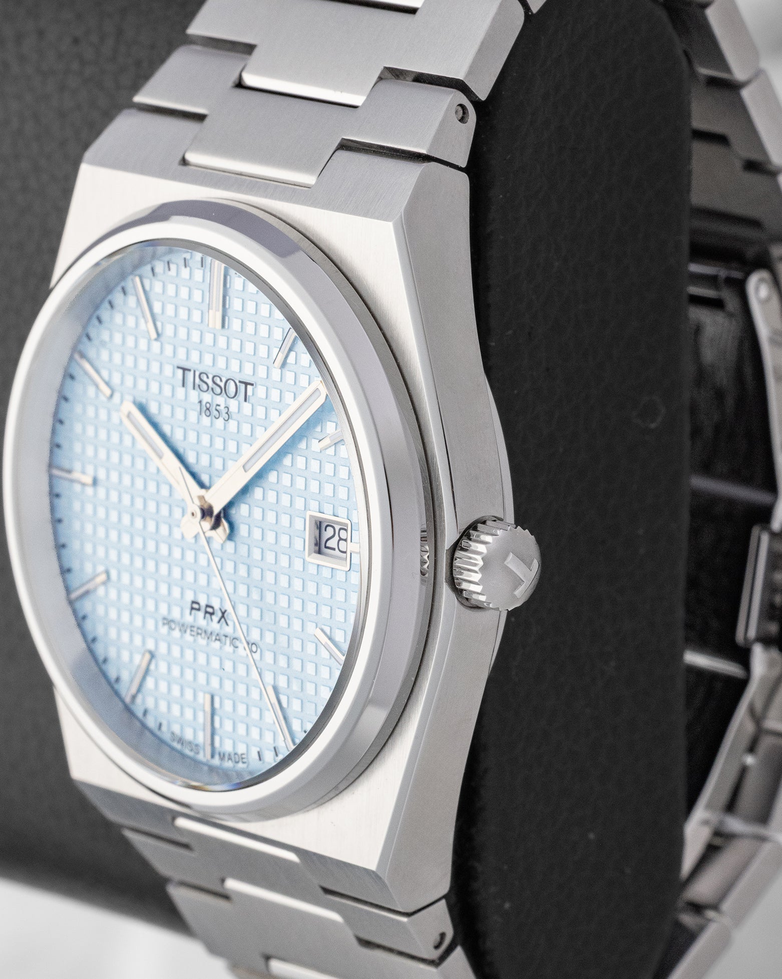 Close-up right side profile of the angular brushed stainless steel Tissot PRX case featuring the T-engraved crown