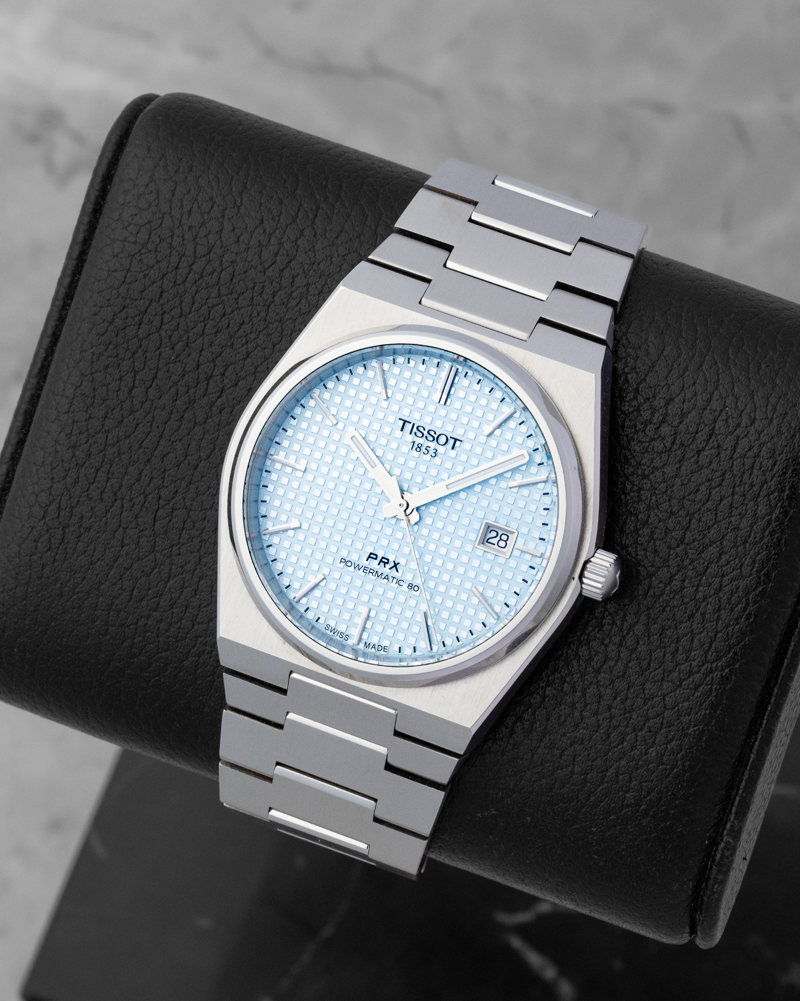 Angled view of the Tissot PRX automatic watch, showcasing the waffle texture dial and light reflecting on the baton indexes