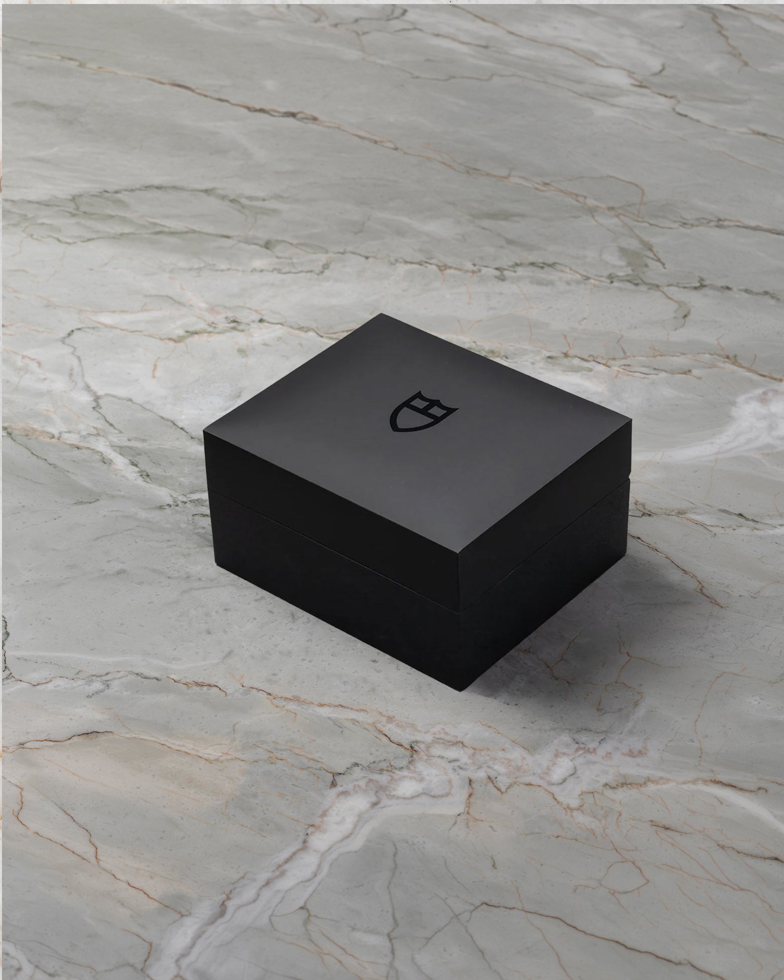 angled overview of the closed textured black Tudor luxury watch presentation box sitting on a stone studio surface