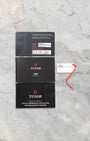 flat-lay view of the official Tudor warranty documentation, METAS certification booklets, and white serial hangtag resting on marble