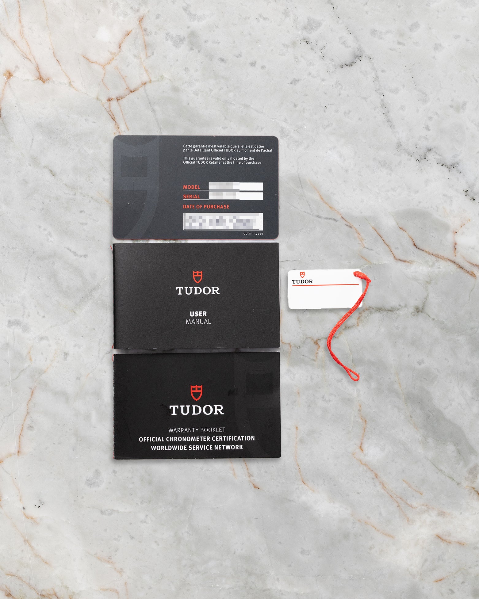 flat-lay view of the official Tudor warranty documentation, METAS certification booklets, and white serial hangtag resting on marble