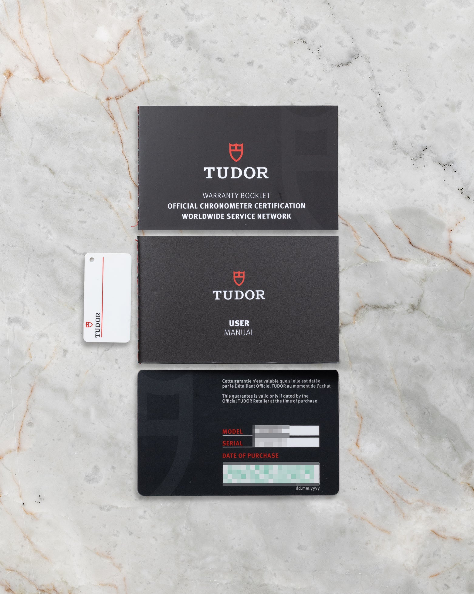 The official Tudor international warranty card, chronometer certification booklet, and user manual laid out on a marble surface