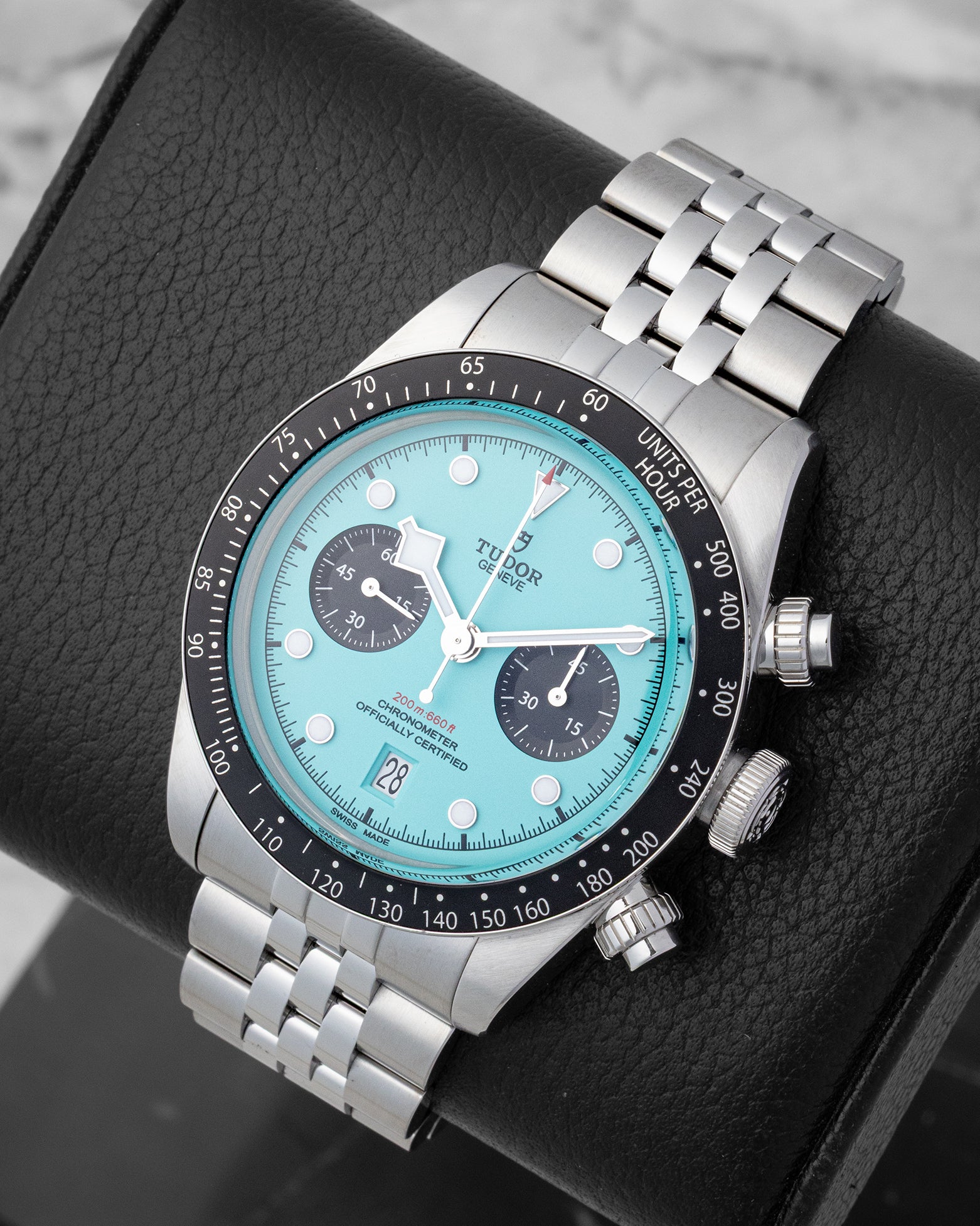 An angled studio profile shot of the 41mm stainless steel Tudor Black Bay Chrono with a pink turquoise dial resting on a leather cushion