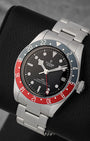 A high-angle three-quarter studio portrait of the 41mm stainless steel Tudor GMT case resting on a black leather cushion to highlight its bidirectional 24-hour graduate scale aluminum bezel