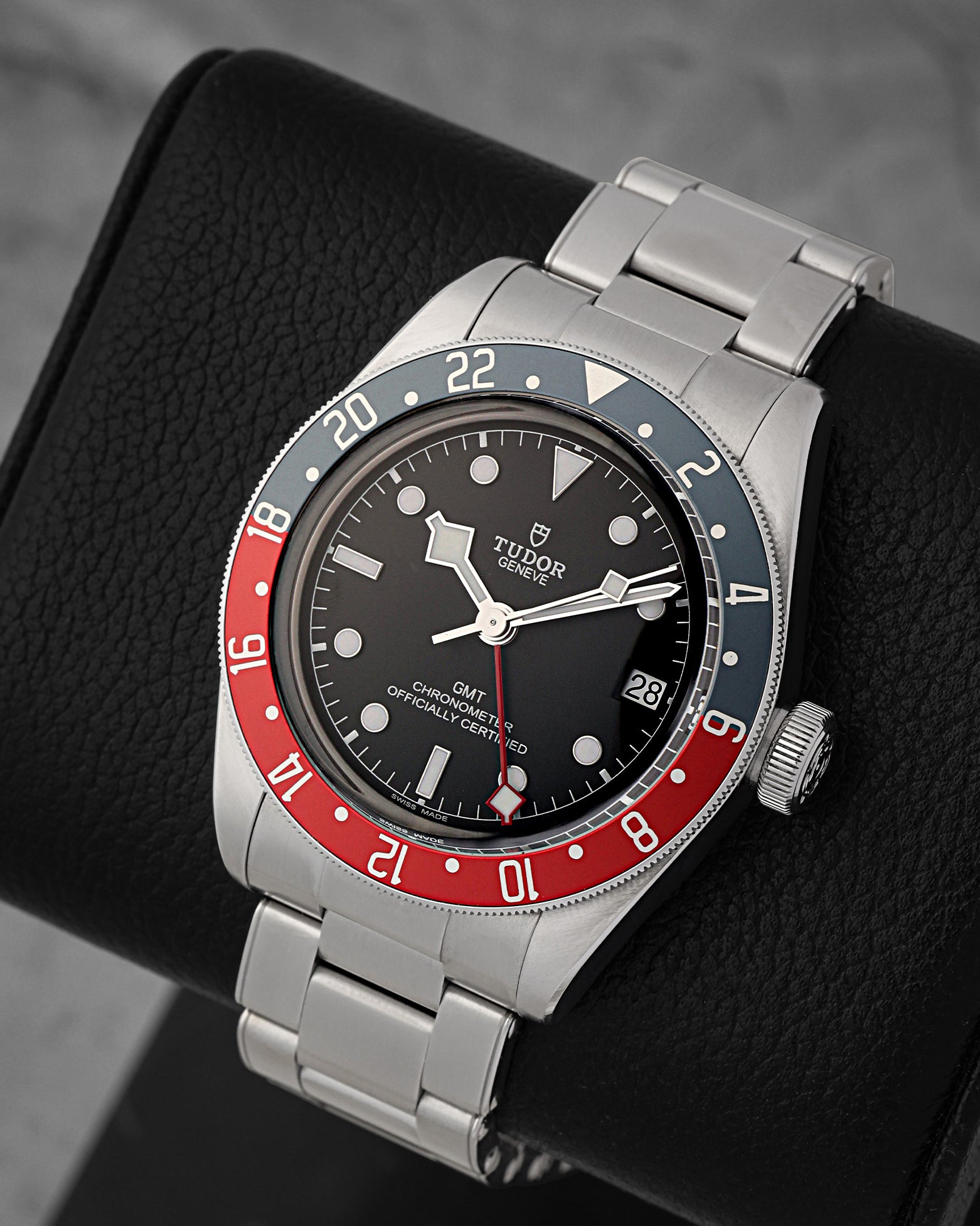 A high-angle three-quarter studio portrait of the 41mm stainless steel Tudor GMT case resting on a black leather cushion to highlight its bidirectional 24-hour graduate scale aluminum bezel