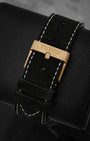 Rear perspective of the black nubuck leather strap with contrast white stitching, secured by a brushed bronze tang buckle engraved with the Tudor logo