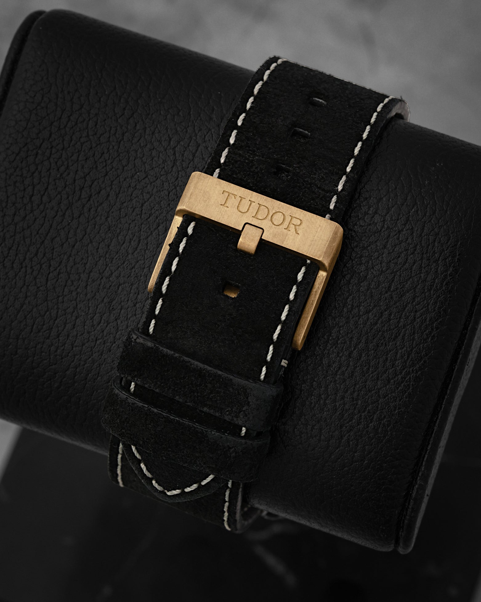 Rear perspective of the black nubuck leather strap with contrast white stitching, secured by a brushed bronze tang buckle engraved with the Tudor logo