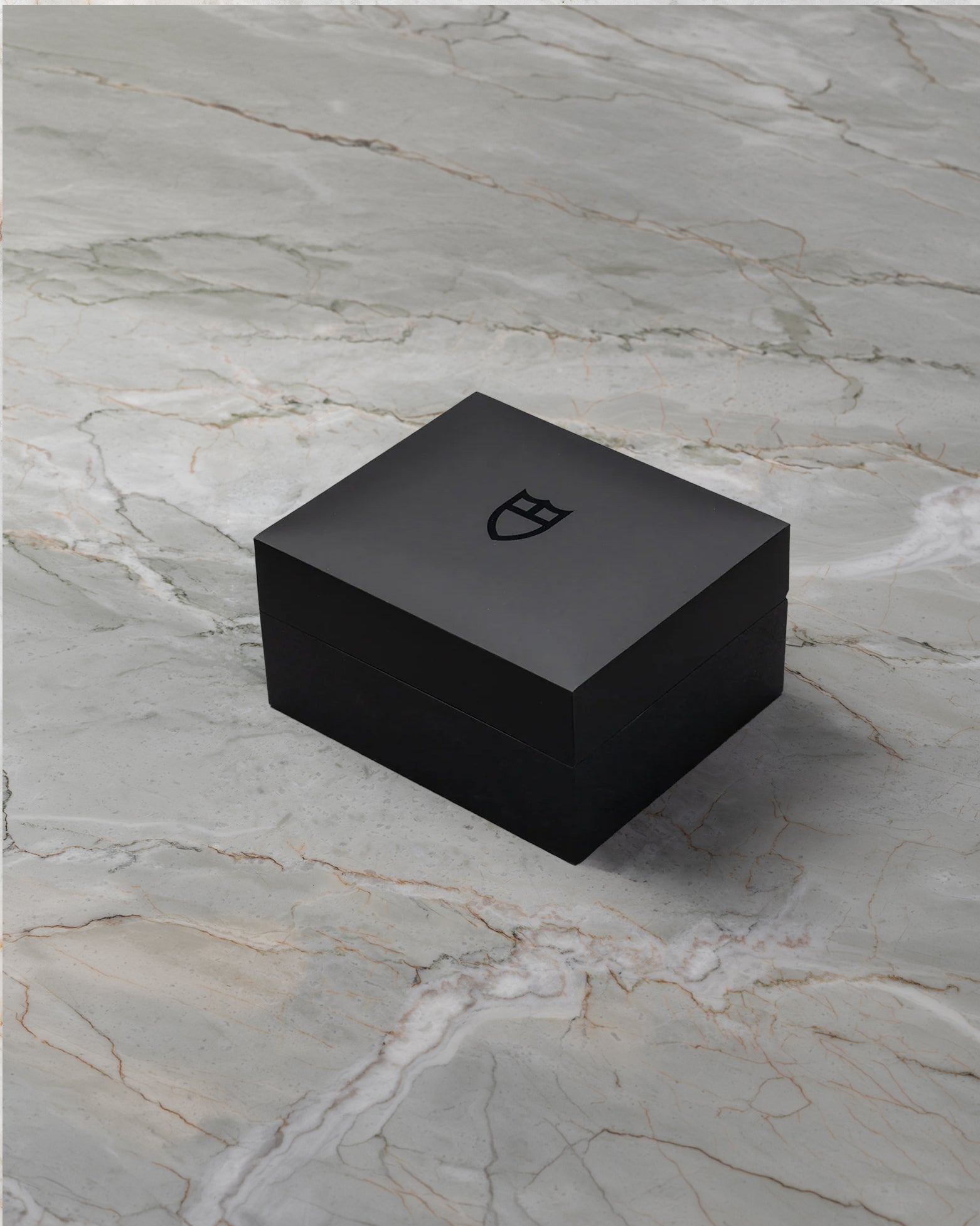 angled overview of the closed, textured black Tudor luxury watch presentation box sitting on a stone studio surface