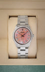 A vintage 1964 Rolex Oyster Perpetual 34 reference 1002 featuring a custom pink MOP dial, diamond hour markers, and a custom diamond-set bezel inside its box at Noah's Fine Watches & Jewelry in Dallas