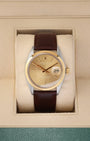 A vintage 1969 Rolex Oyster Perpetual Date reference 1500 featuring a champagne sunburst dial, smooth 14k yellow gold bezel, and a brown leather strap inside its display box at Noah's Fine Watches & Jewelry in Dallas