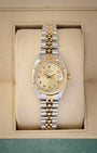 A ladies' vintage 1981 Rolex Lady-Datejust reference 6916 in two-tone 14k gold and steel featuring a champagne dial with printed Roman numeral markers inside its box at Noah's Fine Watches & Jewelry in Dallas