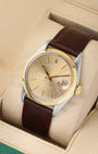 A high-angle three-quarter studio portrait of the 34mm stainless steel and gold Rolex case showcasing the golden baton hour markers and classic open date window layout
