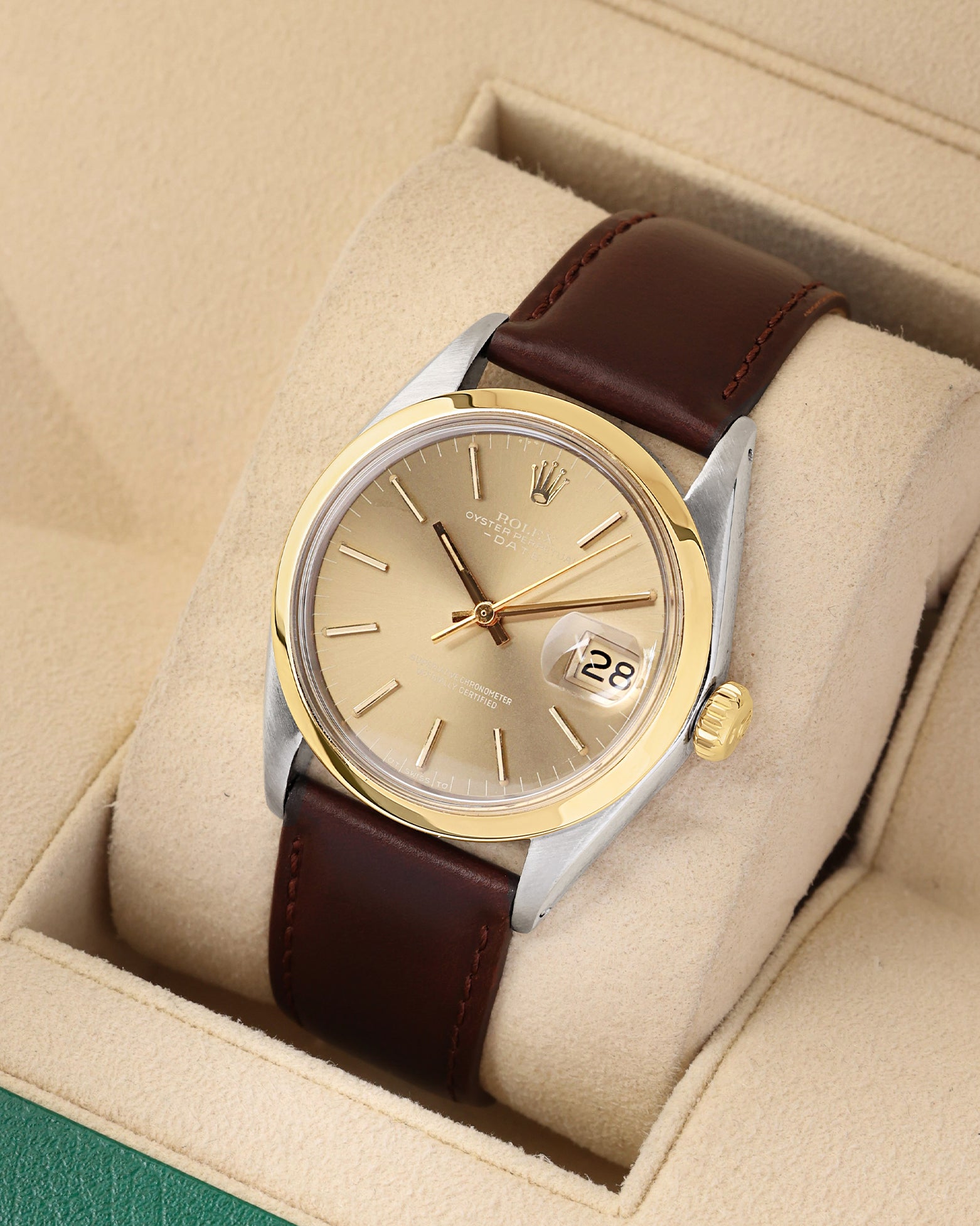 A high-angle three-quarter studio portrait of the 34mm stainless steel and gold Rolex case showcasing the golden baton hour markers and classic open date window layout