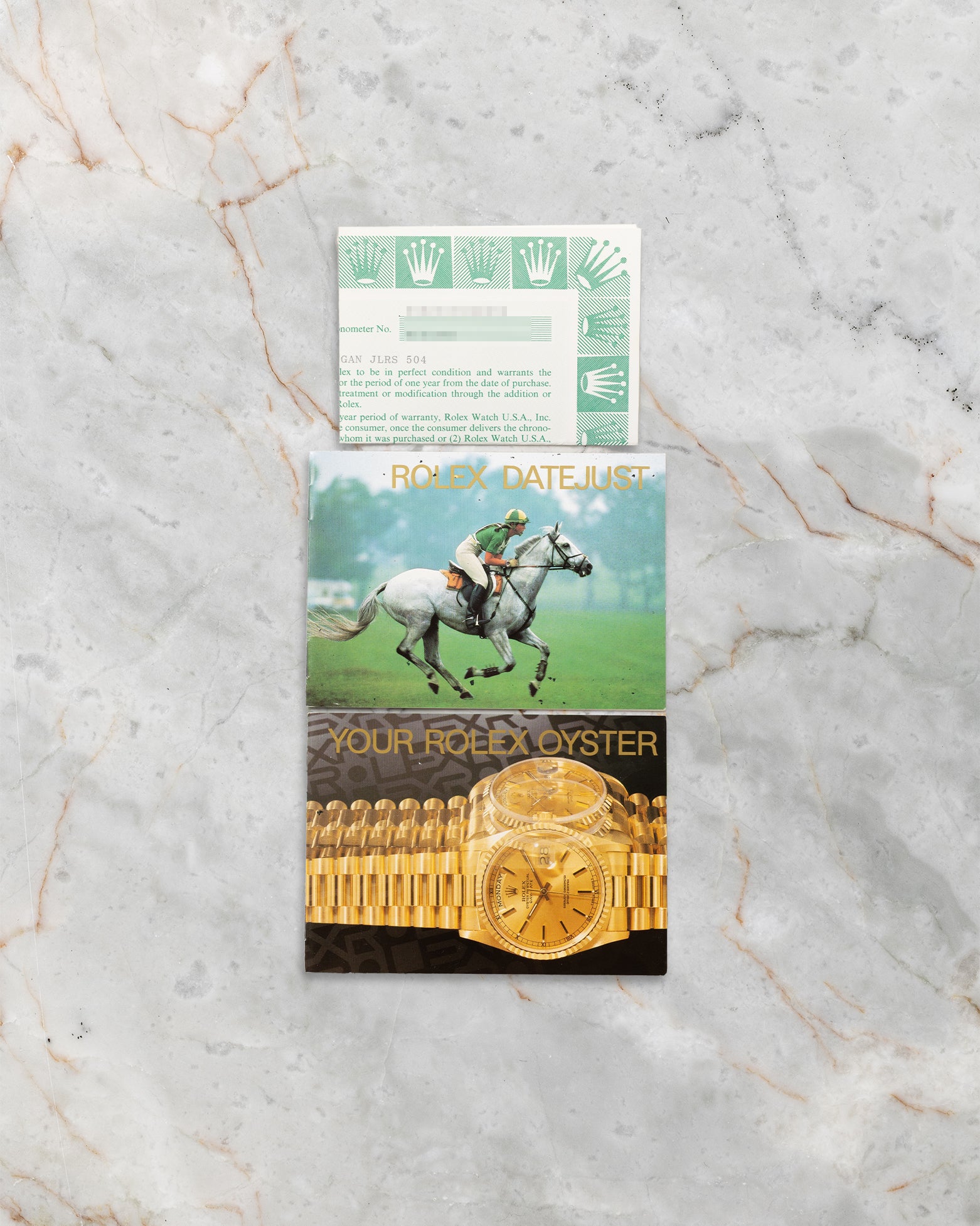 A top-down flat lay view of the original 1988 era printed Rolex user booklet and official punched chronometer certificate papers resting on a grey marble backdrop
