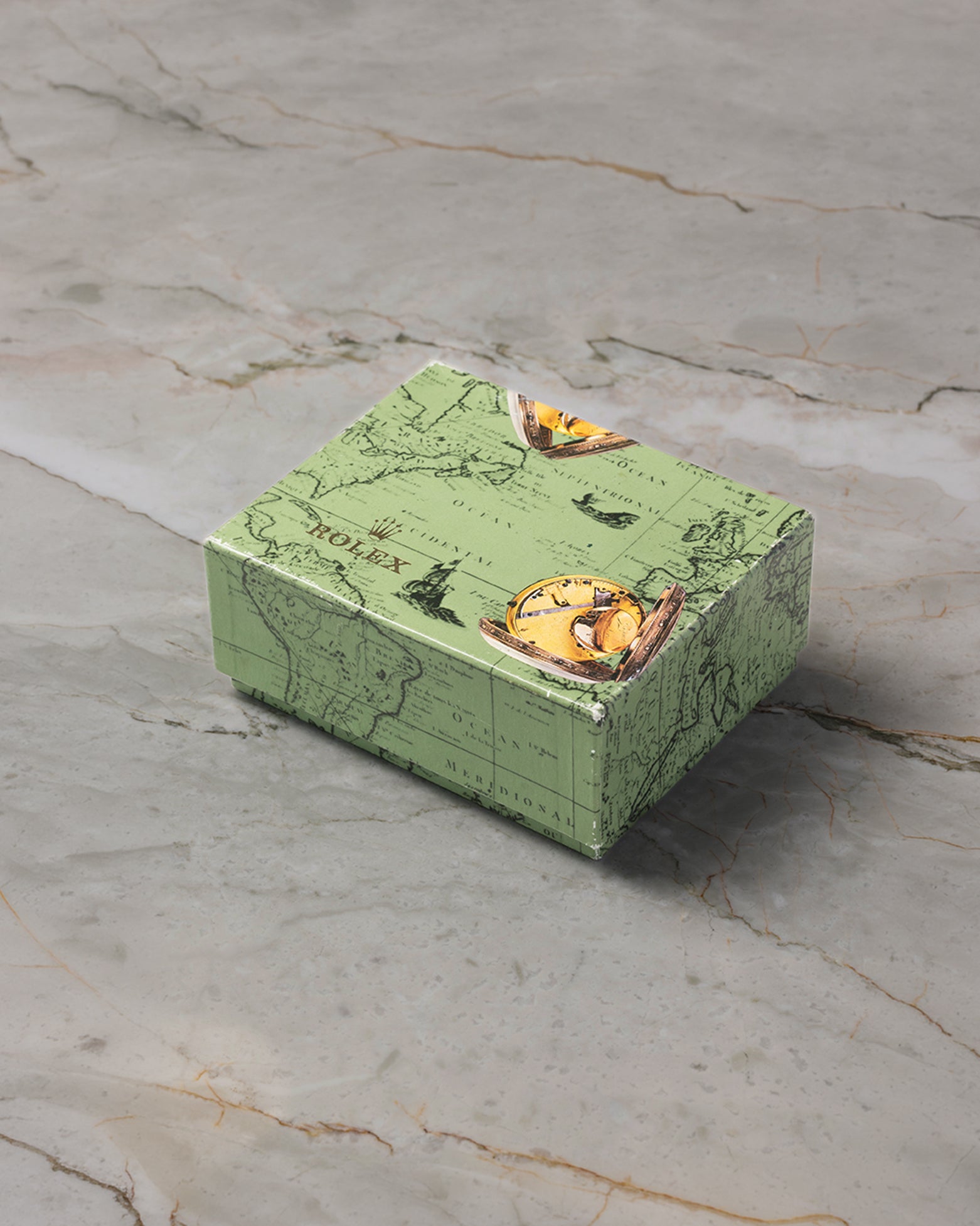 A three-quarter high-angle portrait of the vintage green outer cardboard watch box featuring the historical Rolex crater and oyster shell graphic print