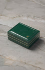 A high-angle shot of the official vintage square green leatherette watch presentation box detailed with gold track border accents resting closed on marble