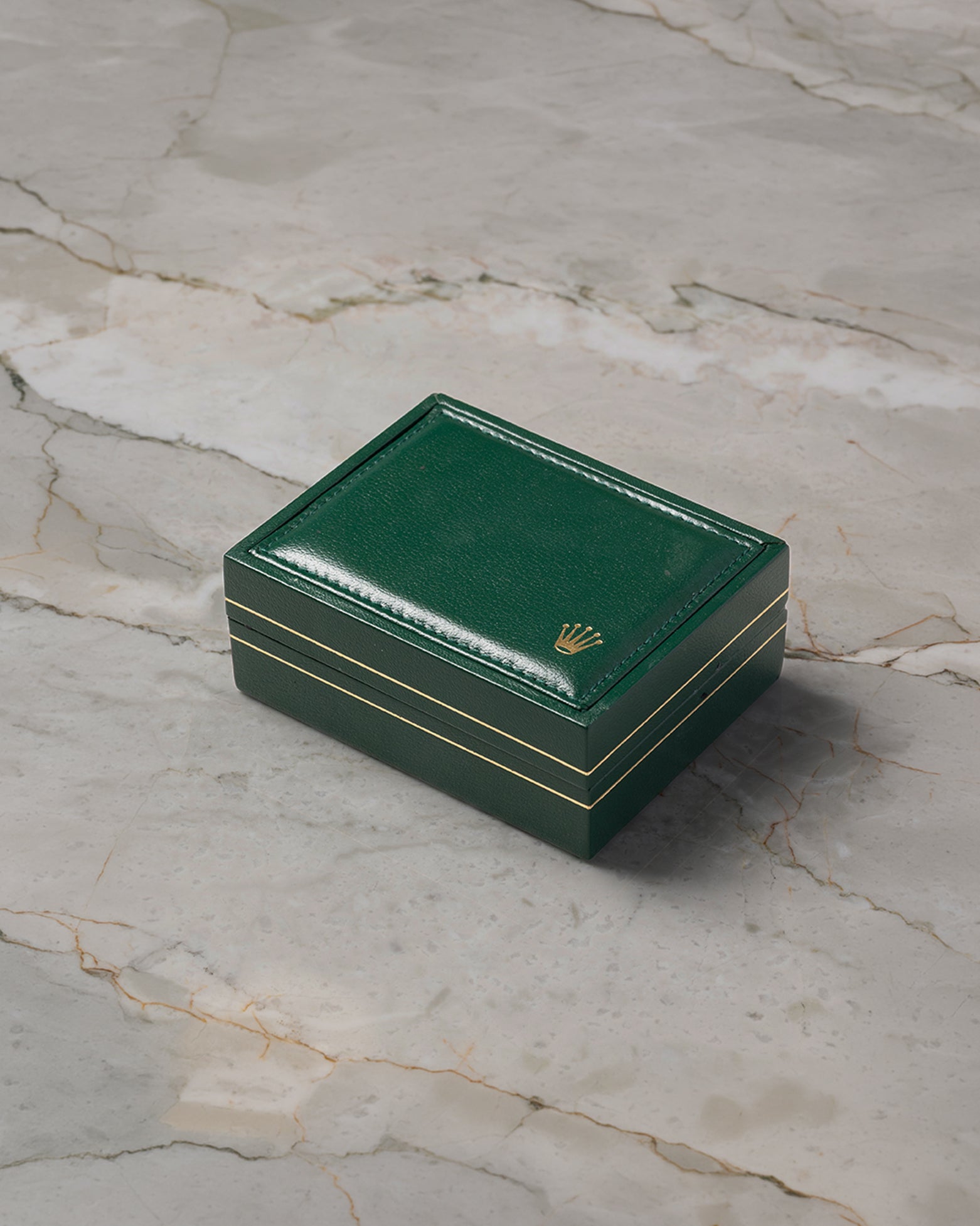 A high-angle shot of the official vintage square green leatherette watch presentation box detailed with gold track border accents resting closed on marble