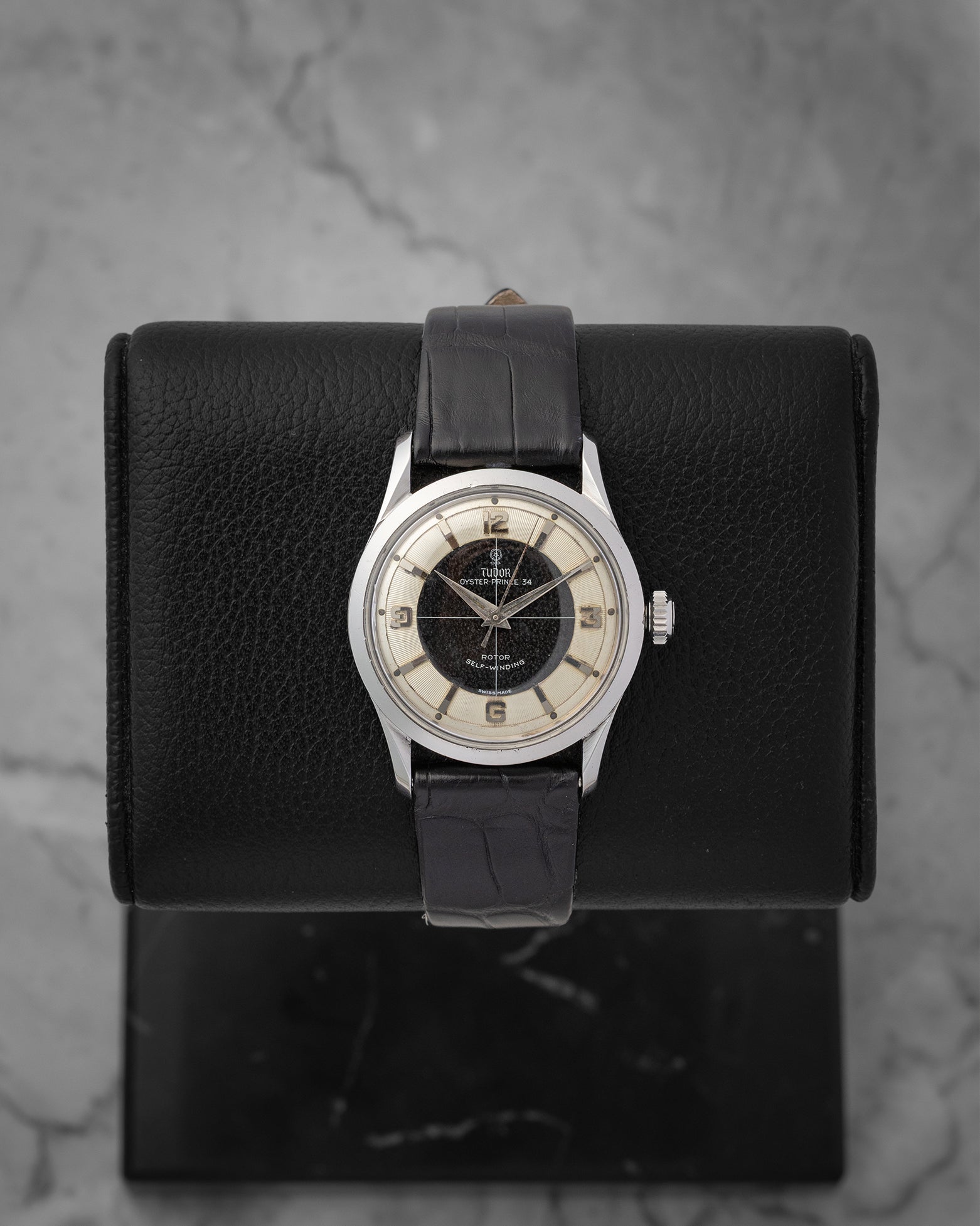 frontal portrait of a vintage 1950s Tudor Oyster Prince 7950 watch with a black and cream Tuxedo sector dial on a leather display mount